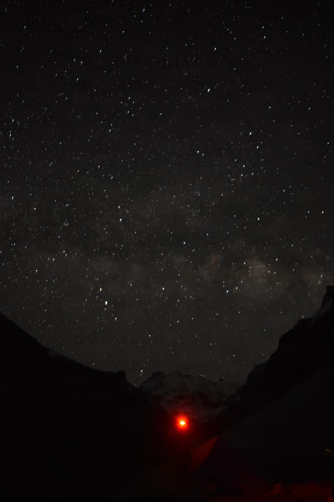 Milky Way emerges above a canyon, crimson headlamp illuminating the vast darkness below.