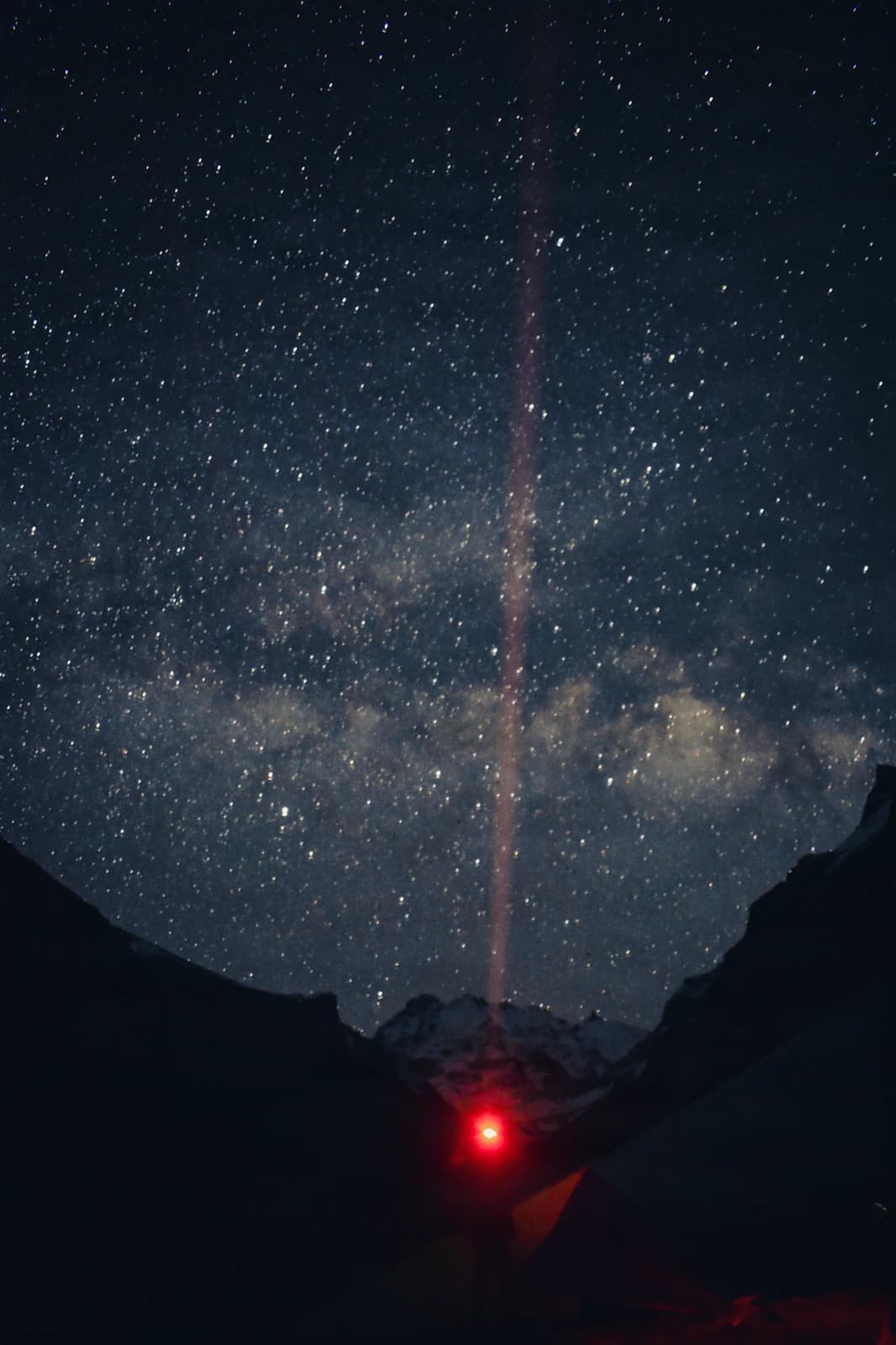 Milky Way's luminous spine rises above silhouetted peaks, anchored by red headlamp glow.