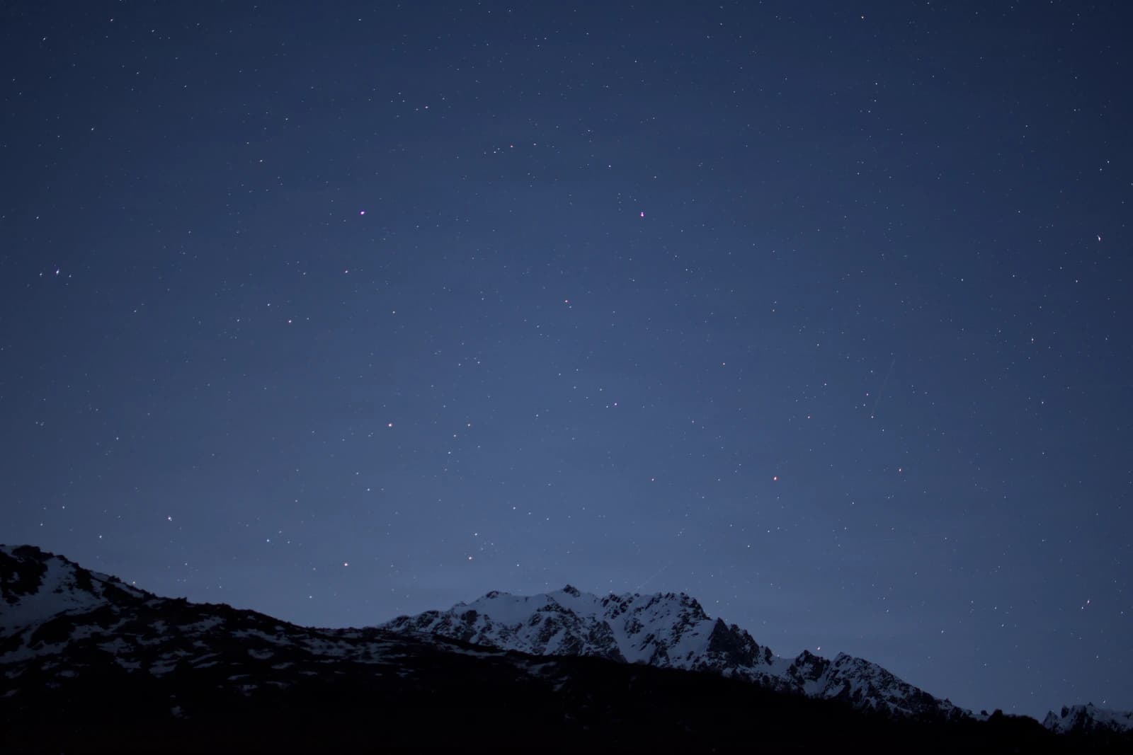 Snow-capped peaks silhouette against deepening twilight's fading blue gradient.