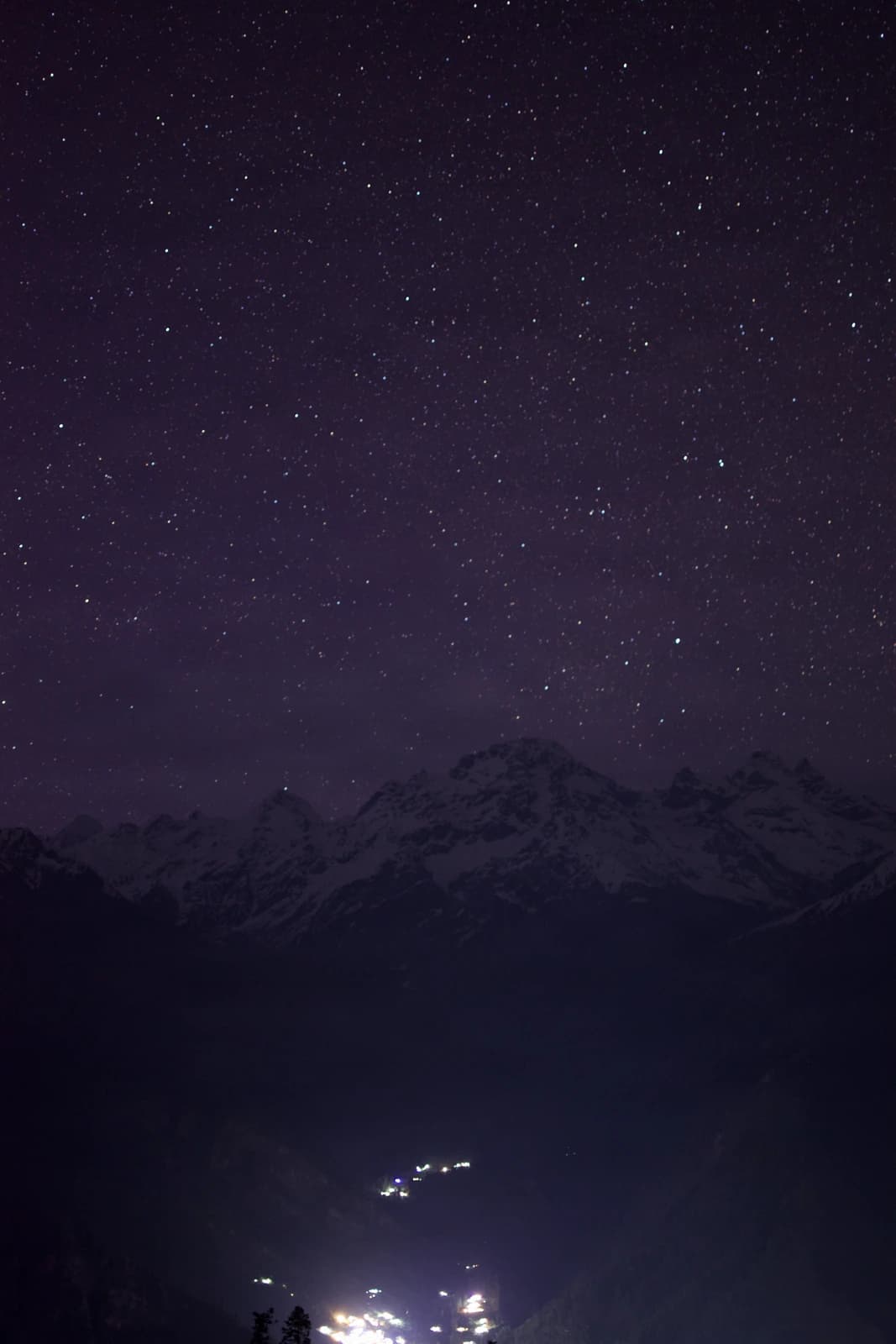 Distant village lights pierce the darkness beneath a star-scattered mountain sky.