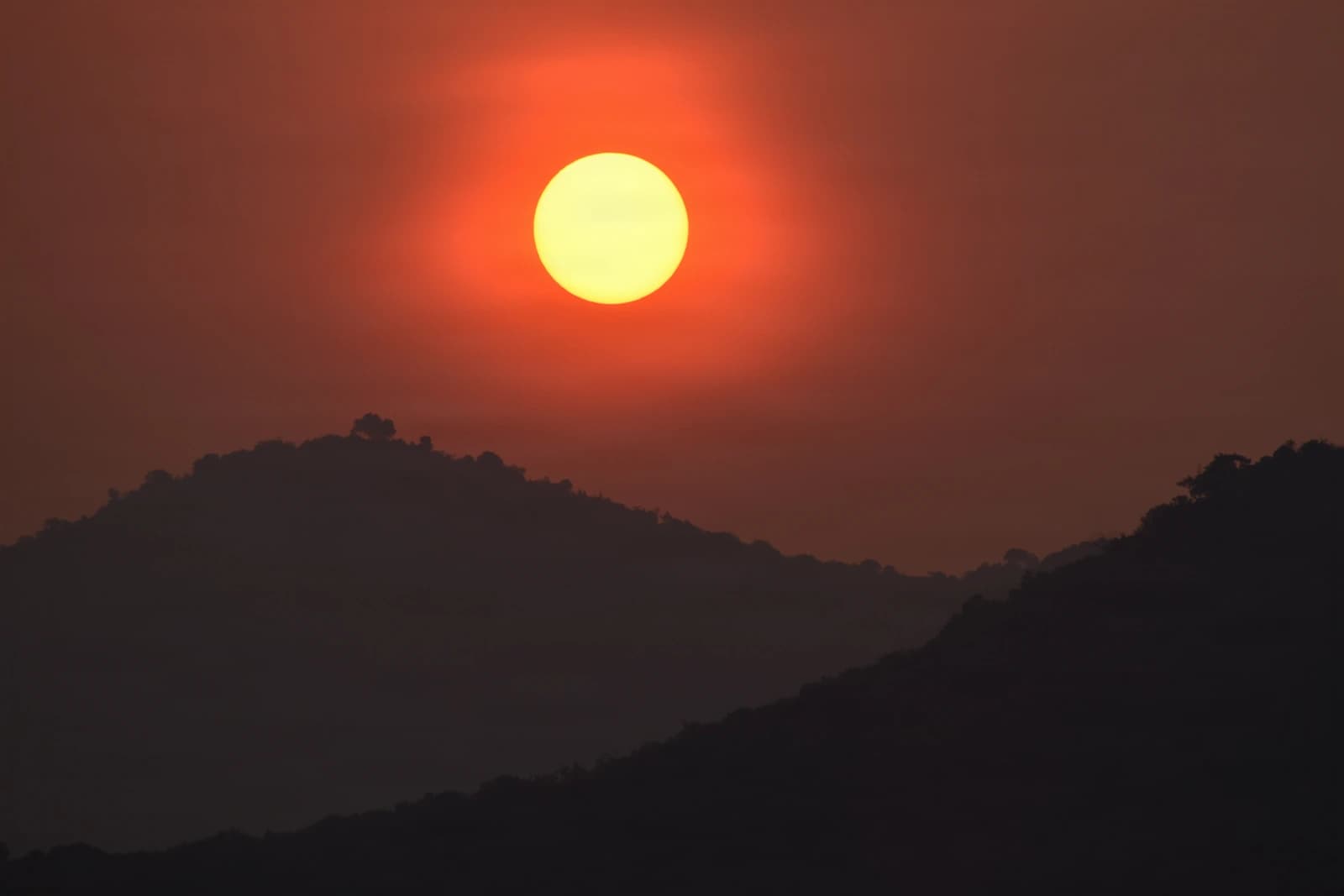 Molten sun sinks between silhouetted ridges in amber stillness.