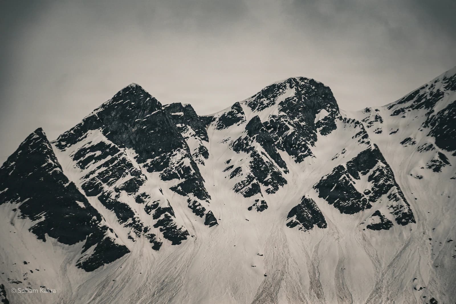 Jagged Himalayan peaks pierce through snow, rock dark against white silence.
