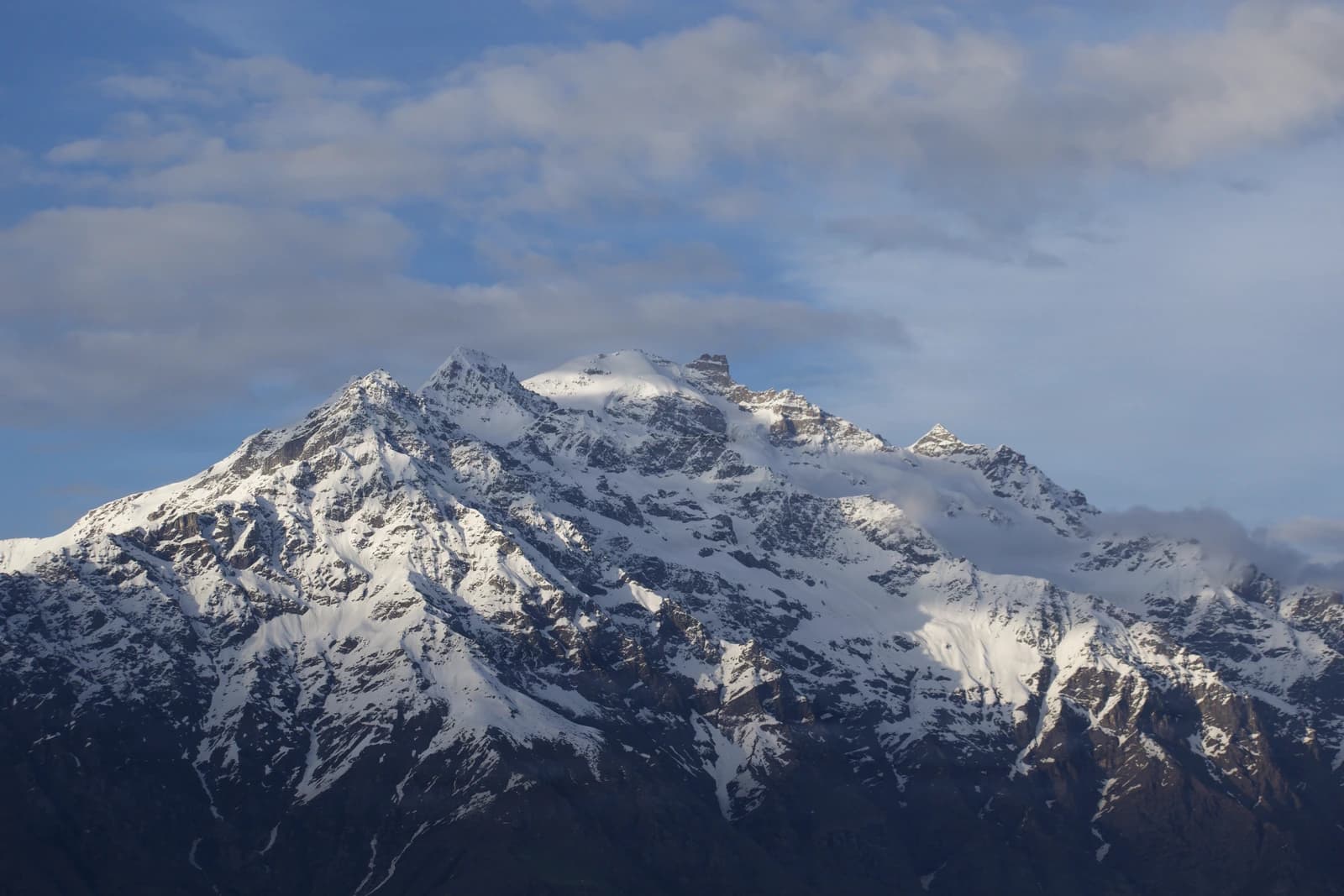 Snow-capped peak pierces scattered clouds above distant foothills.