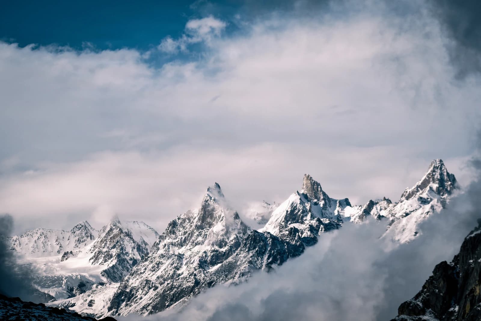 Sharp peaks pierce clouds in a dance of snow and shadow.