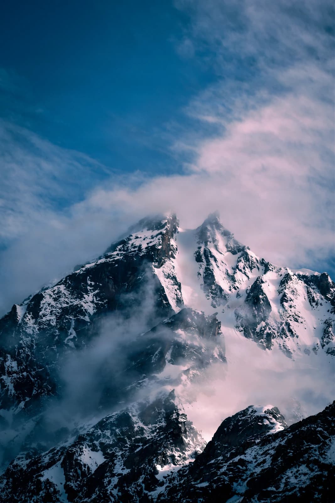 Twin peaks pierce clouds with ethereal light and snow-laden majesty.