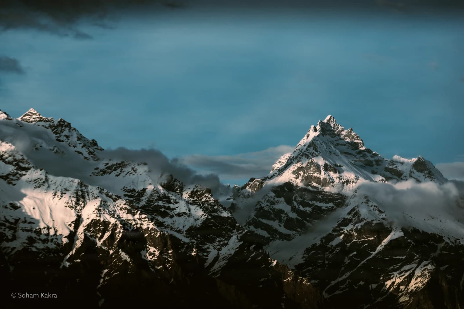Snow-capped peaks pierce turquoise sky, wreathed in gossamer clouds.