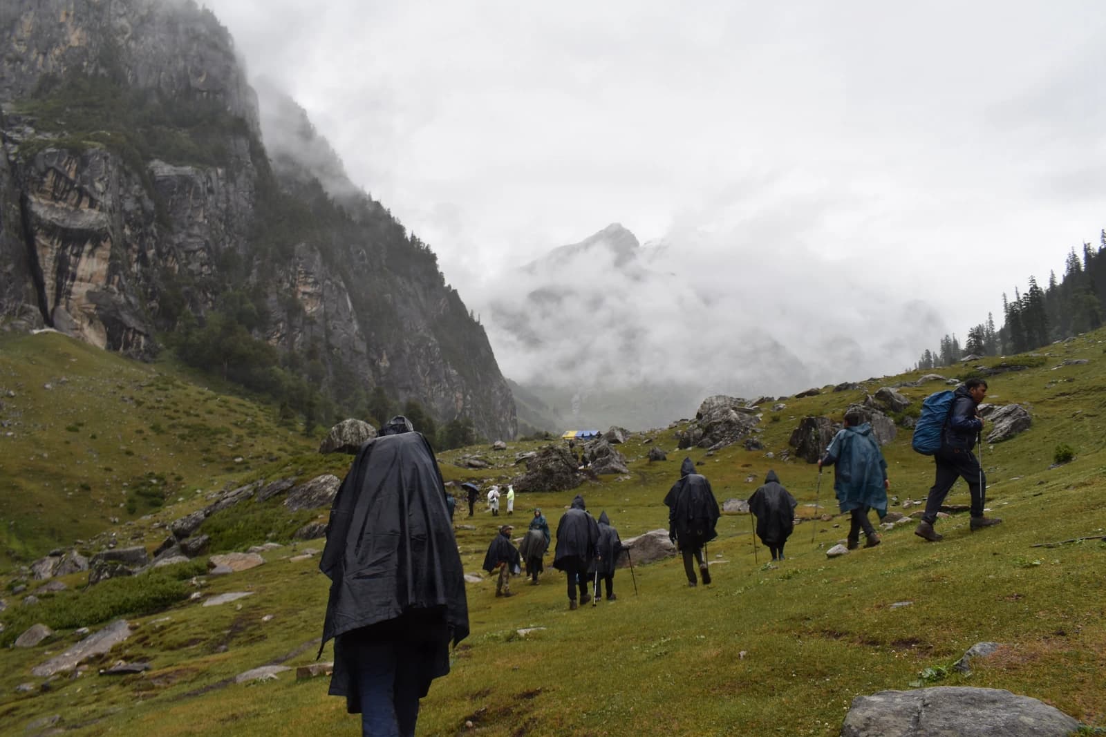 Trekkers traverse mist-shrouded alpine meadow beneath towering limestone cliffs.